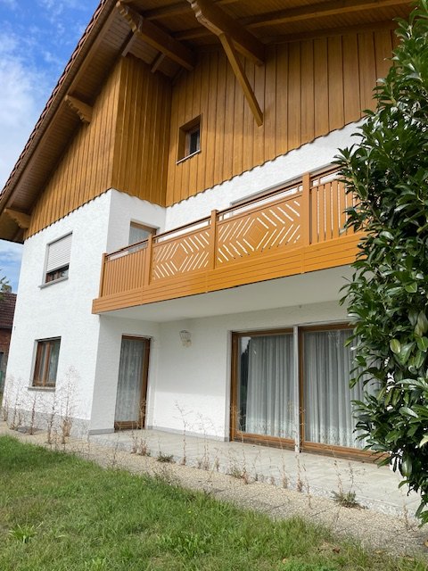 Rückseite des Hauses: weiß verputztes Erdgeschoss mit großen Terrassenfenstern, darüber ein Balkon mit Holzgeländer und eine Lärchenholz-Verkleidung im Giebel.