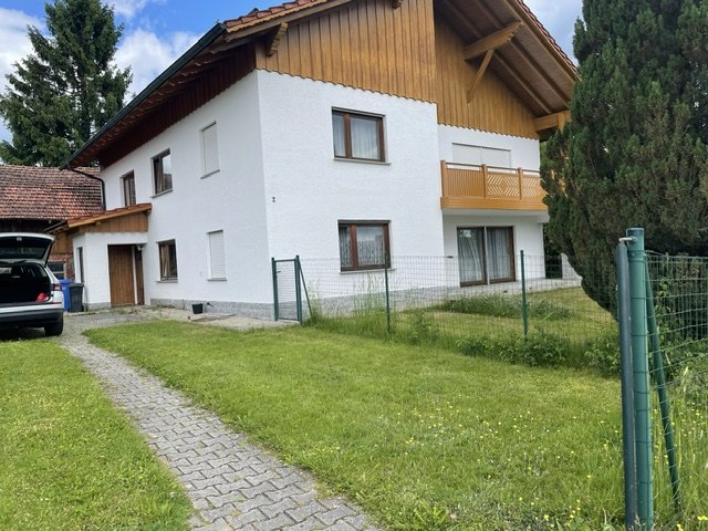 Vorderansicht des Hauses mit gepflastertem Zugangsweg über die Wiese, links Garage und Nebengebäude, rechts der eingezäunte Garten.